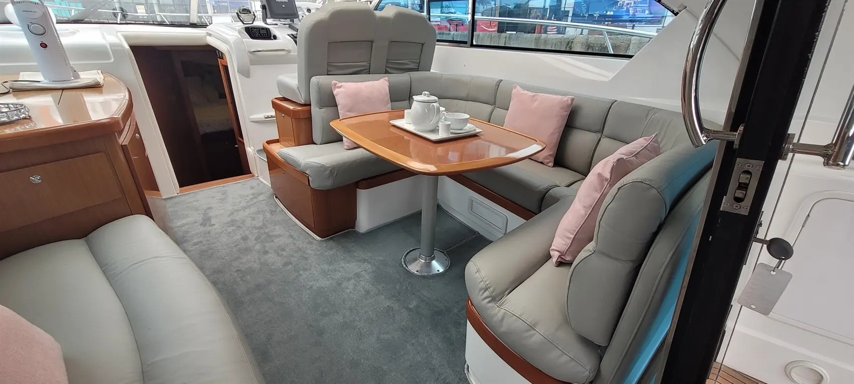 A spacious boat interior featuring grey leather seating, pink cushions, and a wooden table set with a tea service.
